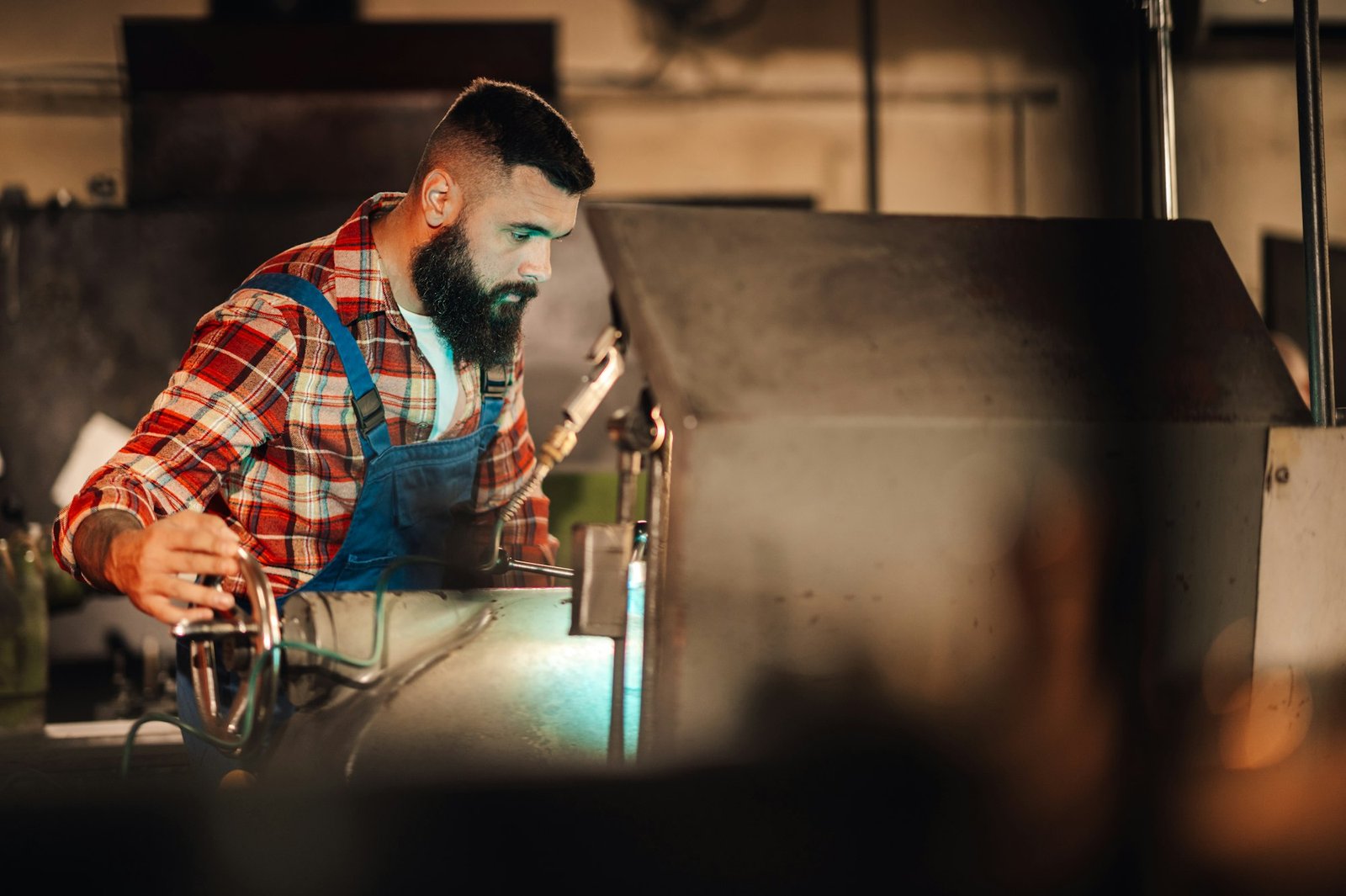 A metal processing worker at work on a lathe machine in a factory.