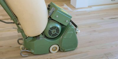 Wooden parquet floor being ground by carpenter using floor sander in a newly constructed home